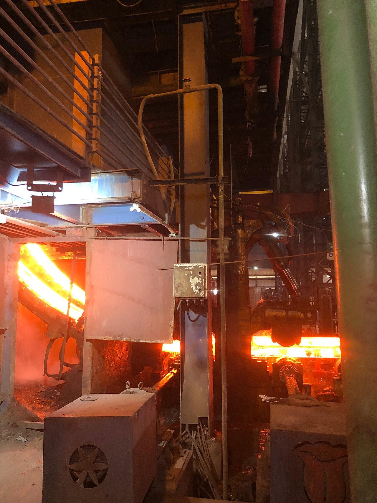 Glowing hot steel bar running through a rolling mill stand